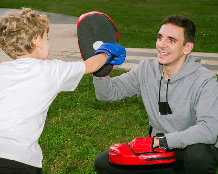 A boxing coach gives a boy a workout in the park