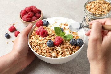 Woman eating tasty granola with berries and yogurt at grey textured table, closeup