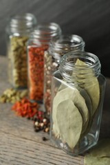 Different spices in glass jars on grey wooden table, closeup