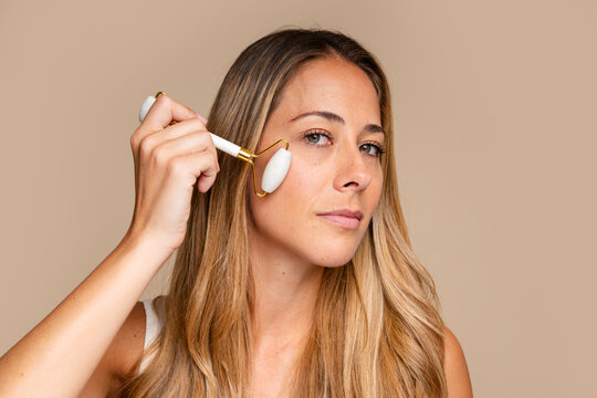 woman using white jade roller for face massage