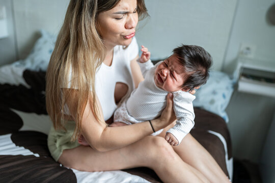 Young mother holding her crying baby on a bed