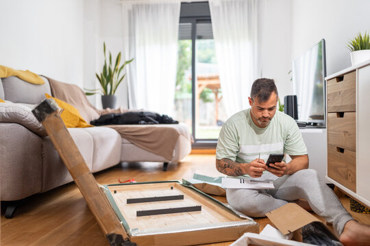 Man assembling furniture while consulting instructions on his phone