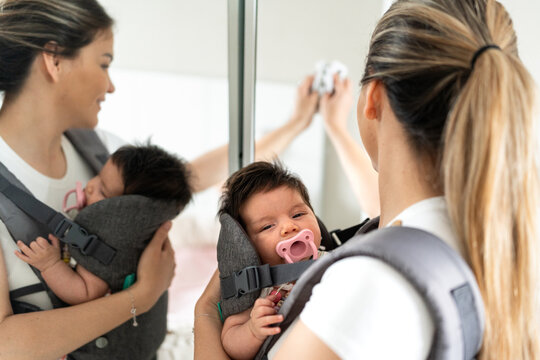Mother holding her baby in a baby sling looking in the mirror