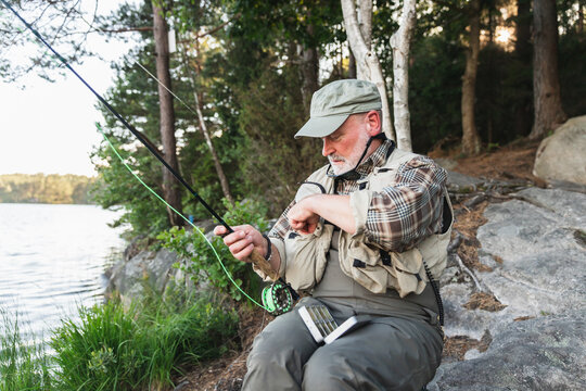 Fisherman Sitting by Lake, Preparing Fishing Hook for Fishing