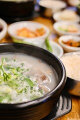 A clay pot of soondae gukbap (blood sausage soup) with steamed rice and assorted banchan, such as...