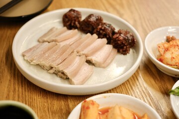 A plate of bossam (boiled pork) and soondae (blood sausage) with assorted banchan (various kinds of kimchi) at Yeodongsik, a Korean gukbap restaurant in Sydney, Australia