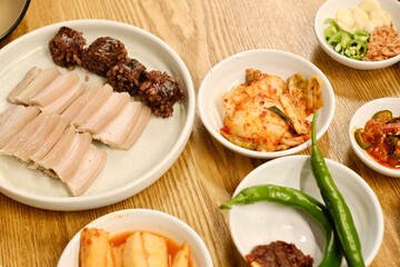 A plate of bossam (boiled pork) and soondae (blood sausage) with assorted banchan (kimchi, pickles, fresh green chillies) at Yeodongsik, a Korean gukbap restaurant in Sydney, Australia