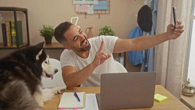 Hispanic man takes selfie with smiling husky in a cozy living room setting.