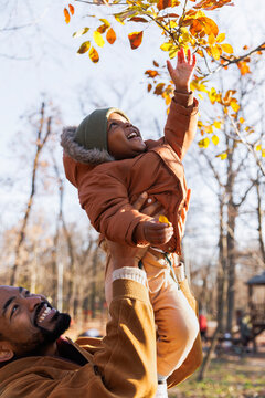 Happy father carrying son touching autumn leaves