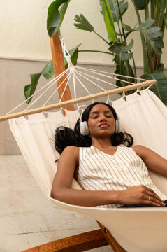 Woman relaxing in a hammock with headphones in tropical indoor setting