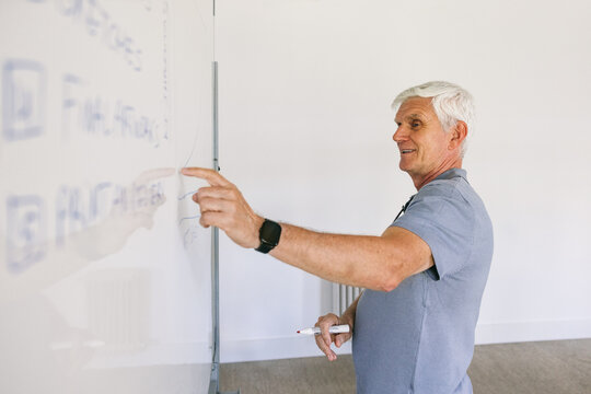 Senior man teaching and writing on a whiteboard in a classroom