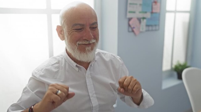 Grey-haired man smiling and dancing in an office, showing a bearded middle-aged senior in a workplace room with indoor light