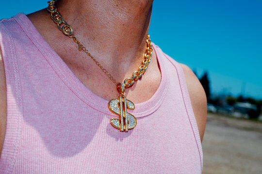 wears a necklace with a pendant in the shape of a dollar symbol