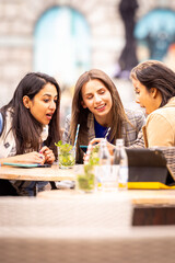 Three friends engage in a lively conversation at an outdoor cafe, enjoying drinks and each others company in the city