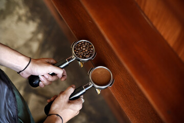 Barista holding ground coffee and beans in portafilter holder against background. Close up.