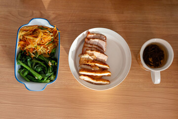 A healthy lunch for a Chinese worker in Asia, featuring grilled chicken and pork with potatoes, choy sum, and other vegetables, all illuminated by natural sunlight, making the meal appear very appetiz