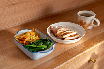 A healthy lunch for a Chinese worker in Asia, featuring grilled chicken and pork with potatoes, choy sum, and other vegetables, all illuminated by natural sunlight, making the meal appear very appetiz