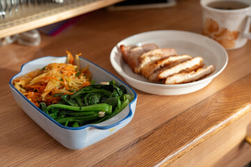 A healthy lunch for a Chinese worker in Asia, featuring grilled chicken and pork with potatoes, choy sum, and other vegetables, all illuminated by natural sunlight, making the meal appear very appetiz