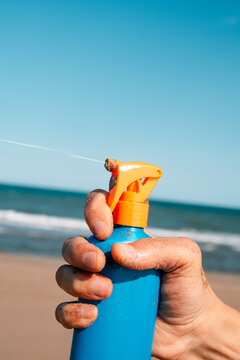 sprays a spurt of sunblock from a bottle on the beach