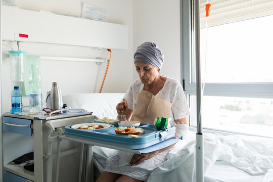 Senior woman eating lunch in hospital bed after chemotherapy