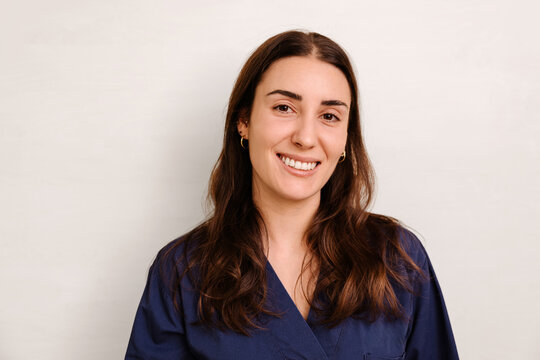 Young woman in blue scrubs smiling at camera with light background