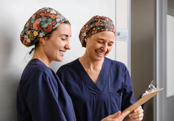 Two medical professionals in scrubs reviewing a clipboard together