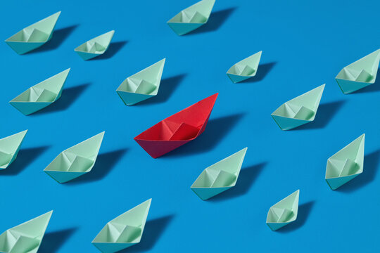 Red Paper Boat Among Green Boats On Blue Background