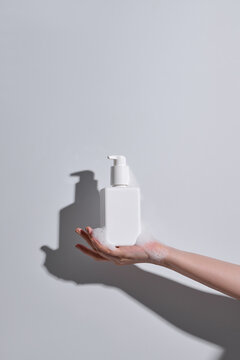 Female hands in foam with white plastic pump bottle on gray background