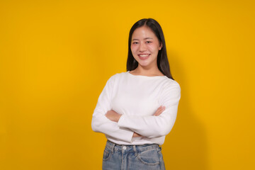 Young woman is standing confidently with her arms crossed, smiling on a vibrant yellow background