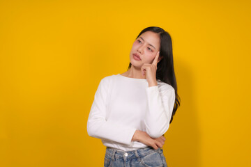 Young woman is standing on a yellow background, deep in thought with her finger on her head