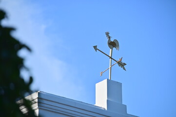 A striking weathervane rooster sits on the roof of a German-style mansion in Anping, Tainan, under a vibrant blue sky, showcasing historical maritime significance.