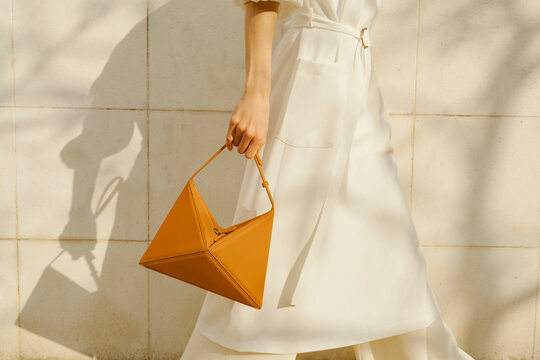 Elegant Woman Holding Geometric Handbag Against Neutral Backgrou