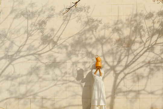 Woman Holding Teapots Over Head Against Shadowy Wall