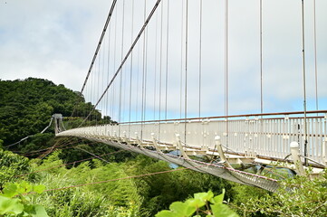 A close-up of the Taiping Suspension Bridge set against a clear blue sky with white clouds on a sunny day. The scene showcases the stunning high-altitude landscape of Taiwan.