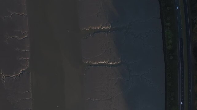 Flagstaff, County Down, Northern Ireland, November 2022. Drone in Bird's Eye pushes north above the Newry river as cars drive along the A2 Warrenpoint Road during an warm winters morning.