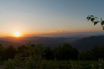 Golden sunset over hills and forests with clear sky.
