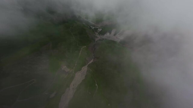 Descending flight through clouds over alpine green meadows. Fast flight down on fpv drone through dense thick clouds