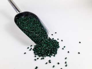 Forest green masterbatch granules in a scoop on a white background.Color pigment carrier polymer in...