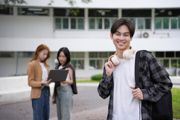 Obraz premium Happy and smiling asian student holding headphones with friends working on a laptop in the background