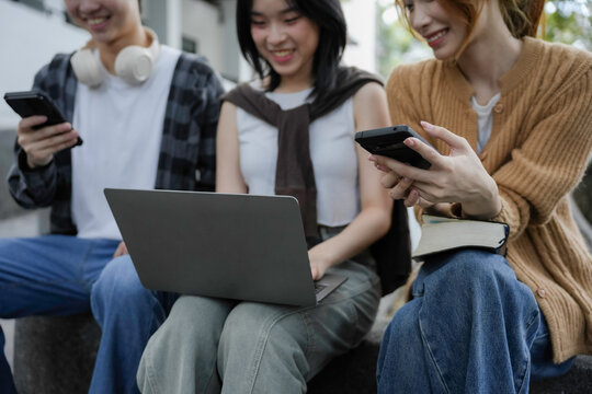 Group of young asian people using technological devices while studying together outdoors