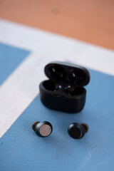 Black modern wireless earphones with case, placed on the basketball court background