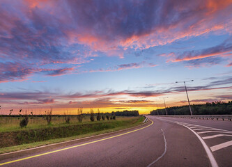 A stunning sunset paints the sky with vibrant colors as a meandering road leads through a serene...