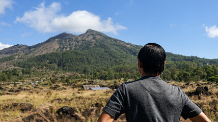 Naklejka premium Back view of a male tourist or traveler looking at Mount Batur in Bali, Indonesia. Beautiful view under a clear sky, perfect for travel and nature themes, highlighting adventure and exploration