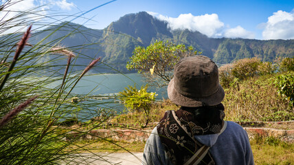 Back view of a male tourist or traveler looking at Mount Batur in Bali, Indonesia. Beautiful view under a clear sky, perfect for travel and nature themes, highlighting adventure and exploration