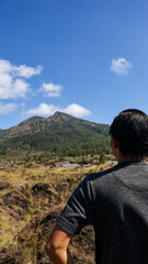 Naklejka premium Back view of a male tourist or traveler looking at Mount Batur in Bali, Indonesia. Beautiful view under a clear sky, perfect for travel and nature themes, highlighting adventure and exploration