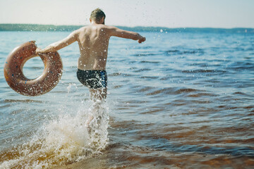 man having fun running into lake holding a rubberswimming ring behaving like a child. regress to...