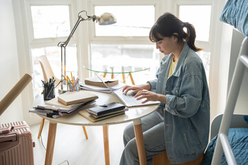Student asian woman sitting on bed in dorm room college student Work or homework on laptop in university dormitory