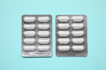 Antibiotic pills in blisters on light blue background, flat lay