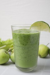 Tasty green smoothie in glass with lime and apples on white tiled table, closeup