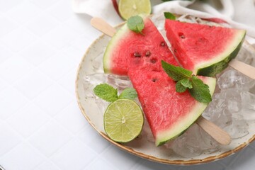Pieces of tasty watermelon, ice cubes, lime and mint on white tiled table, closeup. Space for text